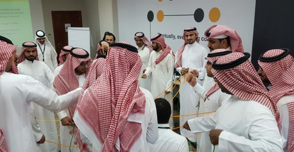 Participants in traditional attire standing in a circle, coordinating with ropes during a collaborative team-building activity.